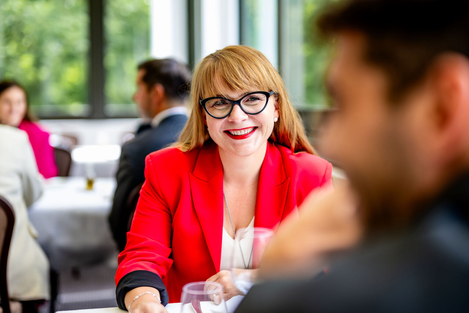 Clientèle élégante déjeunant au Vieux Bois à Genève : femme en blazer rouge souriante.